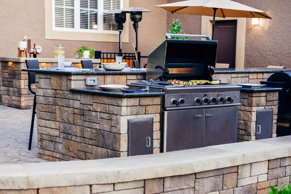 Stone clad outdoor kitchen island with granite counters and a built in grill on a finished patio