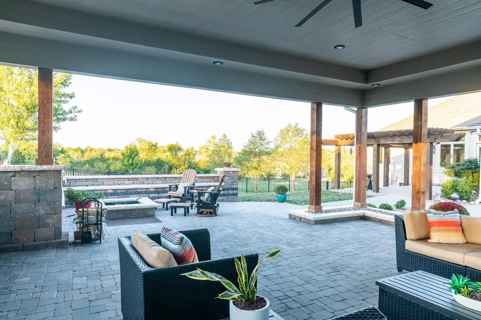 Covered paver patio with cedar posts, a gas fire pit, tiered seat walls and string lighting at golden hour